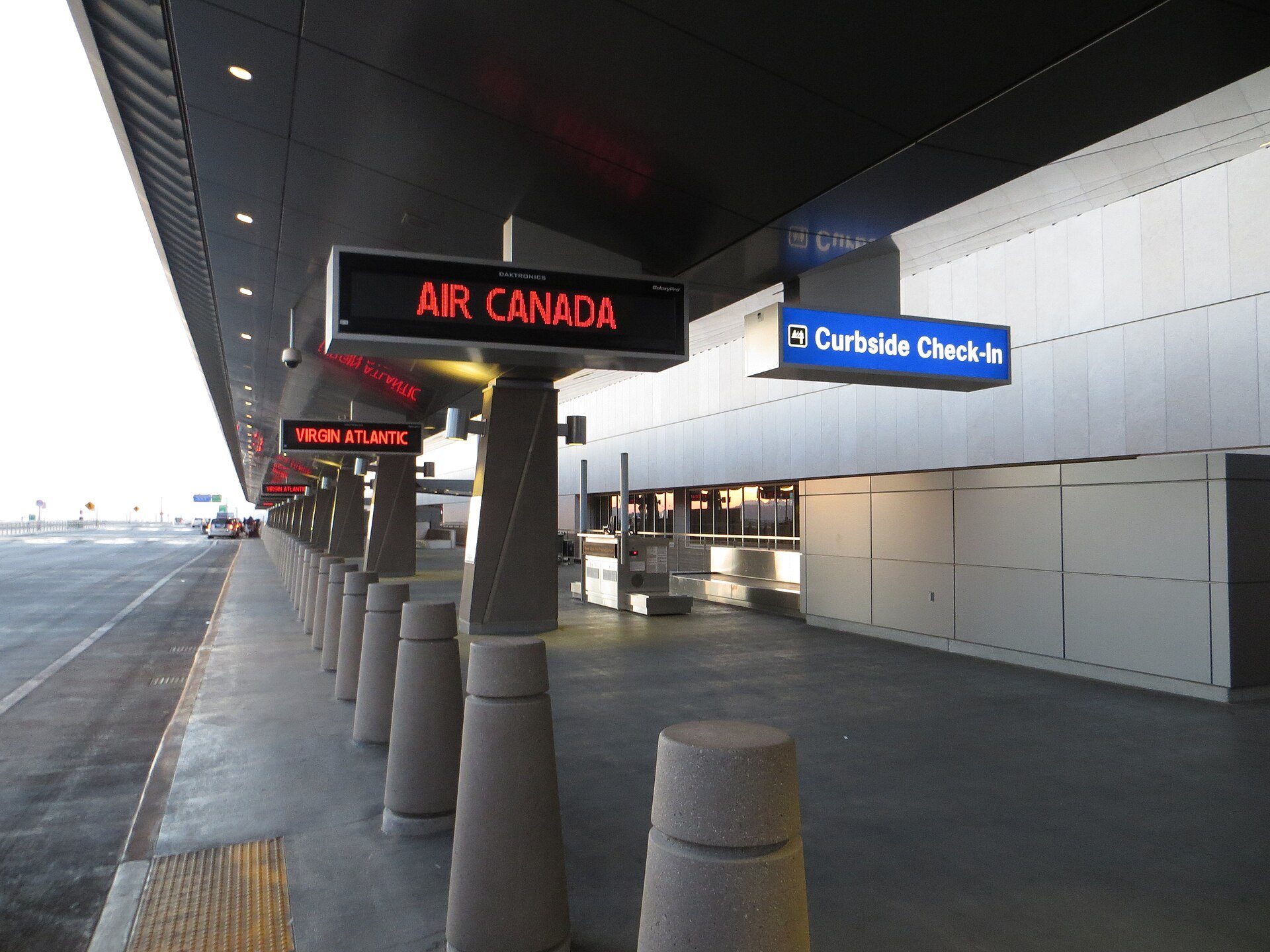 Curbside check-in sign and airline displays along an airport curb